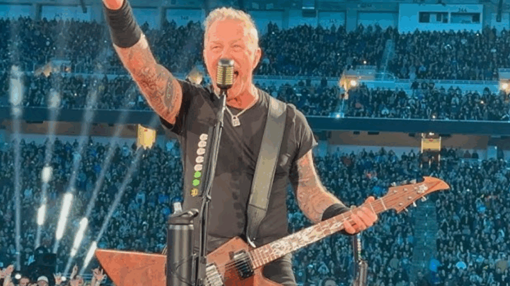 James Hetfield performs live with Metallica during the M72 World Tour in front of a packed stadium crowd, holding his guitar and singing into the microphone.