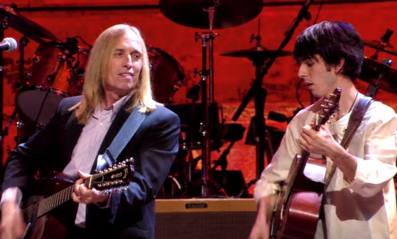 Tom Petty and Dhani Harrison playing acoustic guitars on the red-lit Concert for George stage