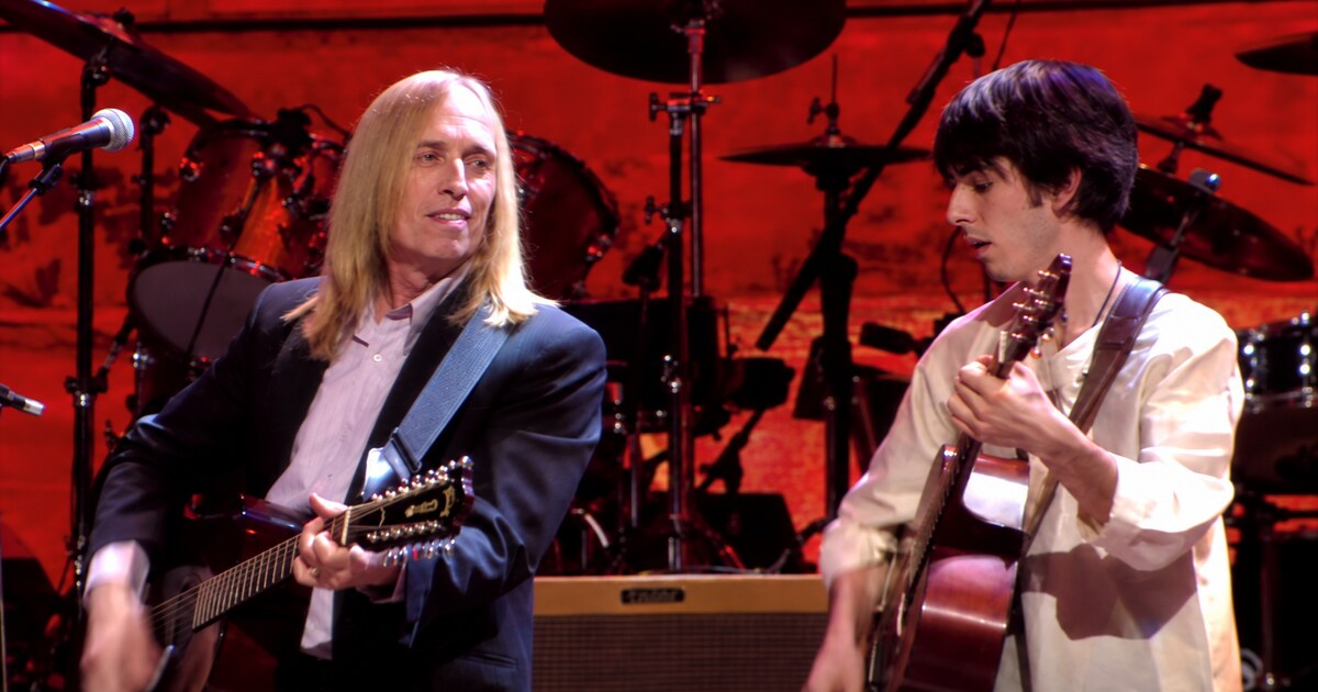 Tom Petty and Dhani Harrison playing acoustic guitars on the red-lit Concert for George stage