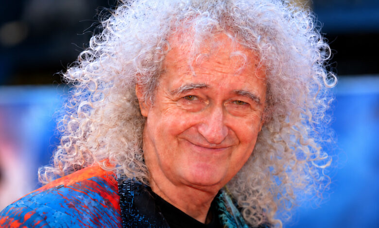 Brian May smiling, with white curly hair and a colorful shirt
