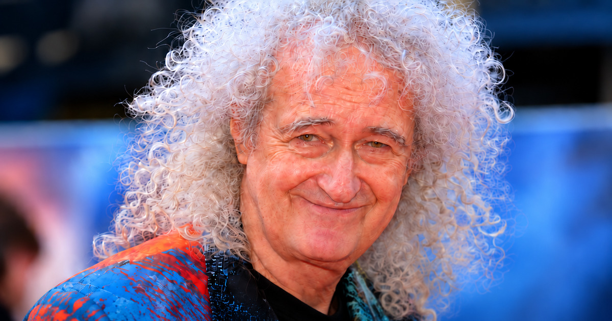 Brian May smiling, with white curly hair and a colorful shirt