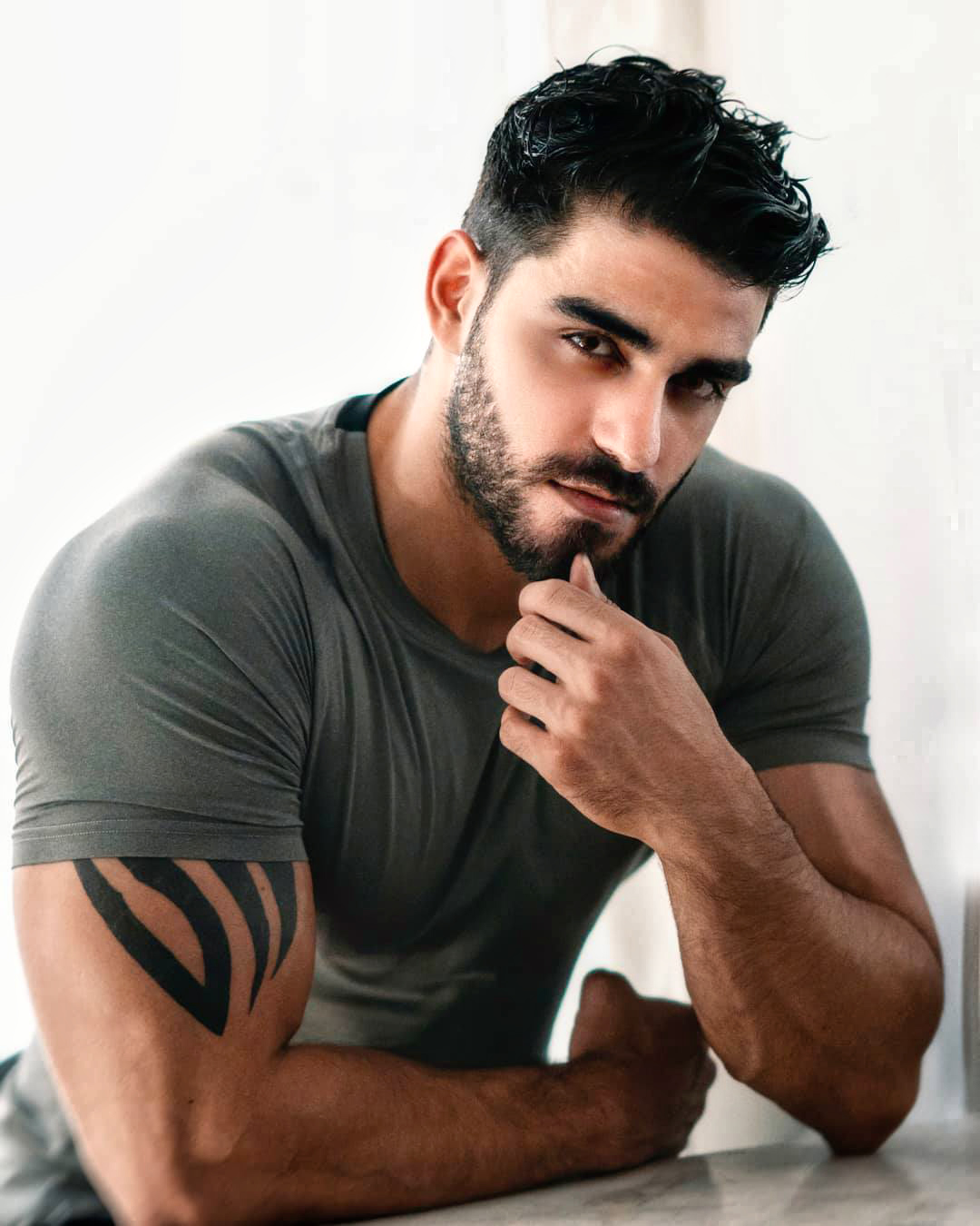 Firat Zan wearing a grey T-shirt, seated with his hand near his chin