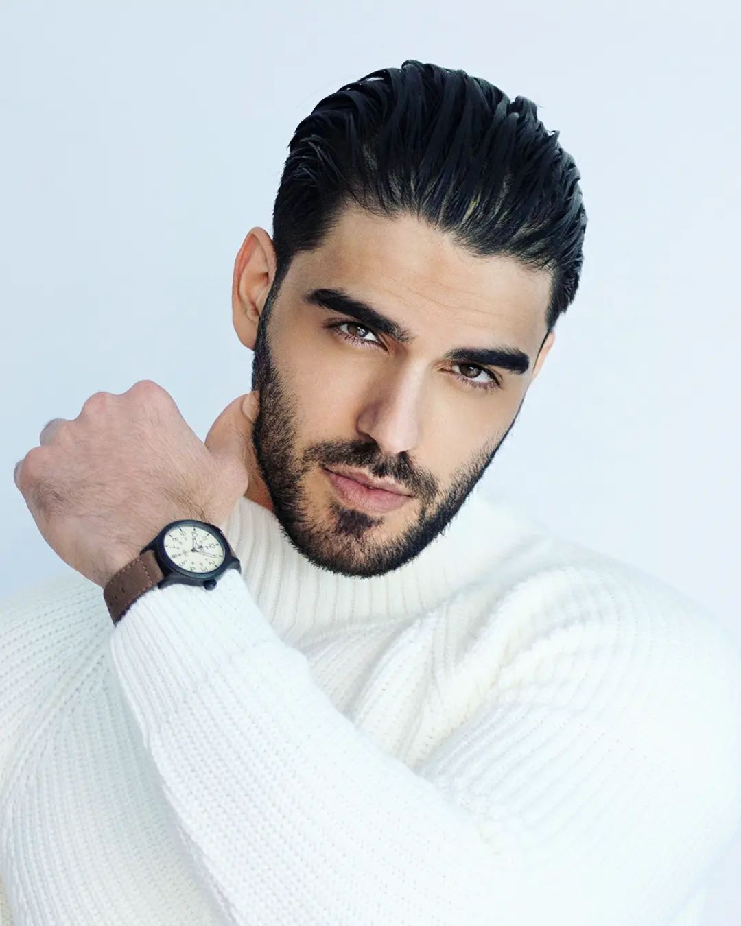 Firat Zan wearing a white cable-knit turtleneck and wristwatch against a pale background