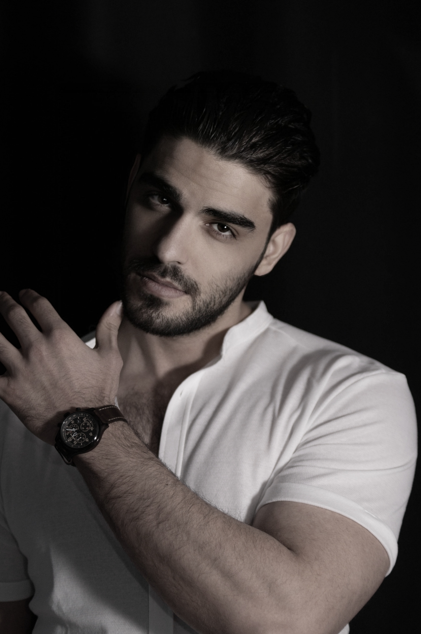 Firat Zan in a white short-sleeved shirt with a wristwatch against a dark background