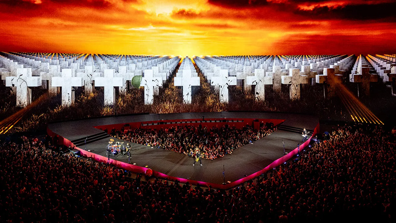 Metallica onstage at Sphere, with the audience beneath a screen showing white crosses and a fiery sky.