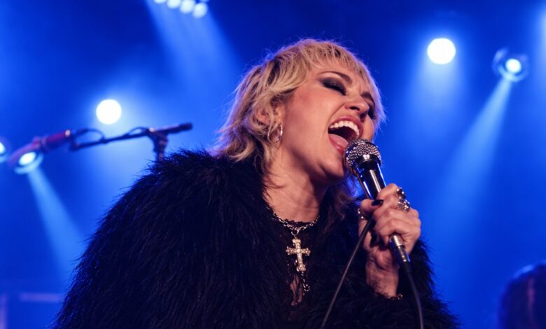 Edited image of Miley Cyrus singing into a microphone on a blue-lit stage.