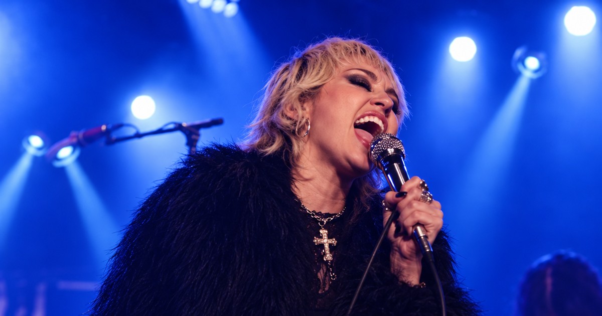 Edited image of Miley Cyrus singing into a microphone on a blue-lit stage.