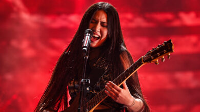 Edited concert image of NeNe Royal singing and playing guitar under red lighting