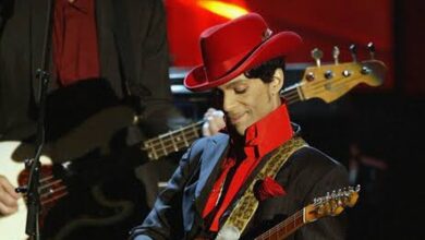 Prince in a red hat performing with his guitar.