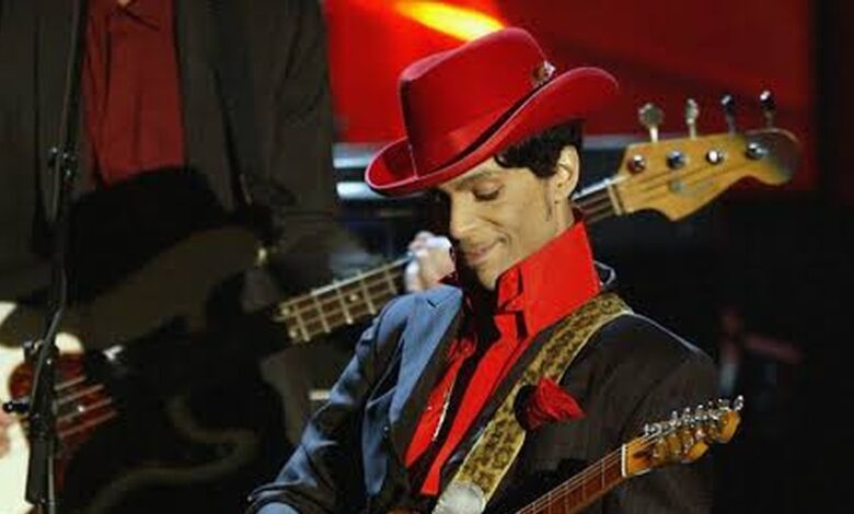 Prince in a red hat performing with his guitar.