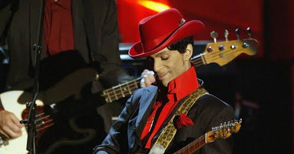 Prince in a red hat performing with his guitar.